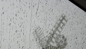 Deszczowa pogoda za oknem. W tle stary drewniany wiatrak. Szyba pokryta licznymi kroplami wody.