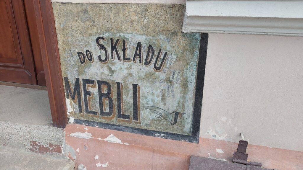 Stary szyld z napisem "Do Składu Mebli" obok drzwi kamienicy na rogu ulic Szczęśliwa oraz Zielony Rynek.